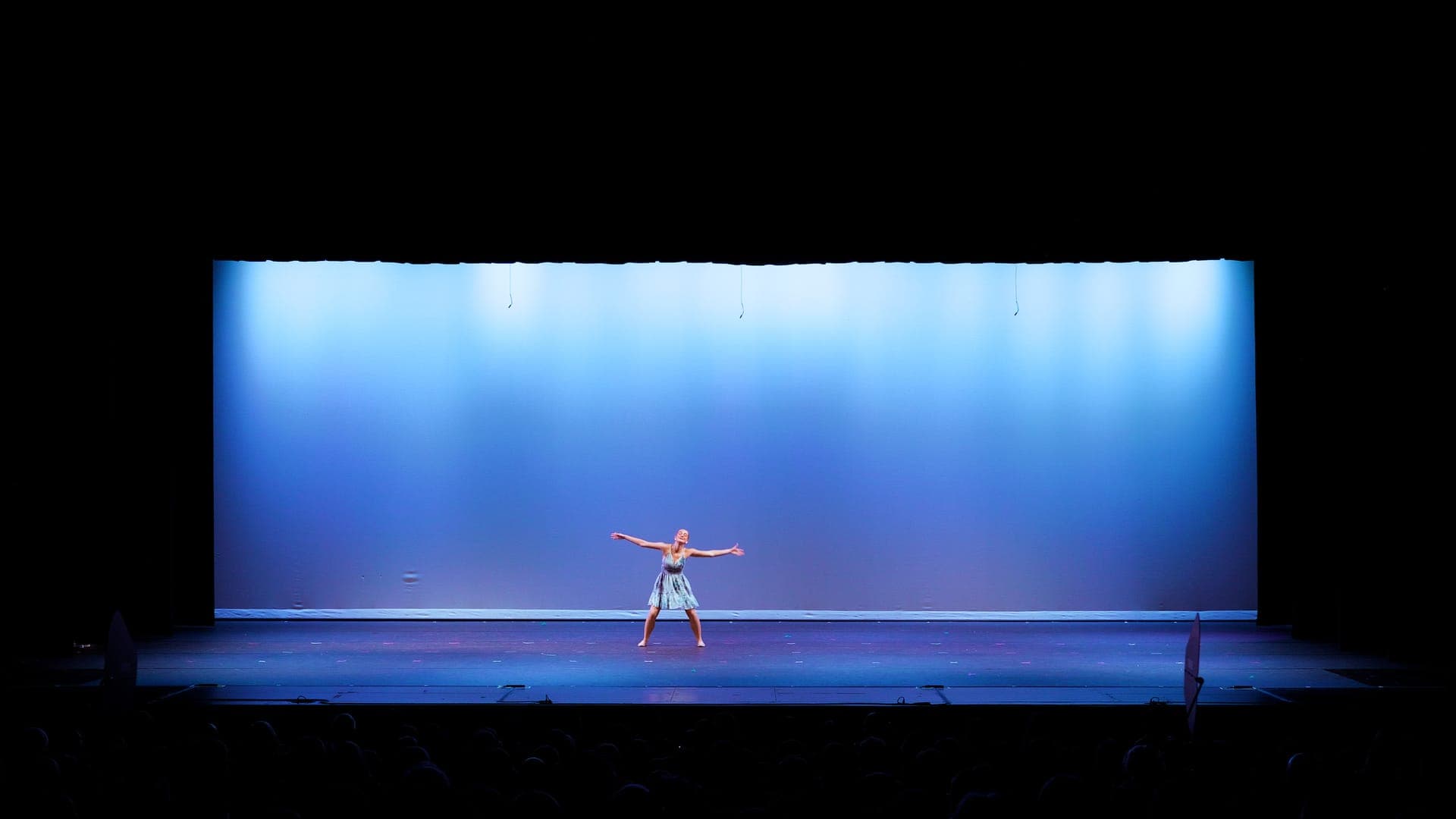 Solo dancer with arms outstretched under a blue spotlight at a St. Louis dance recital