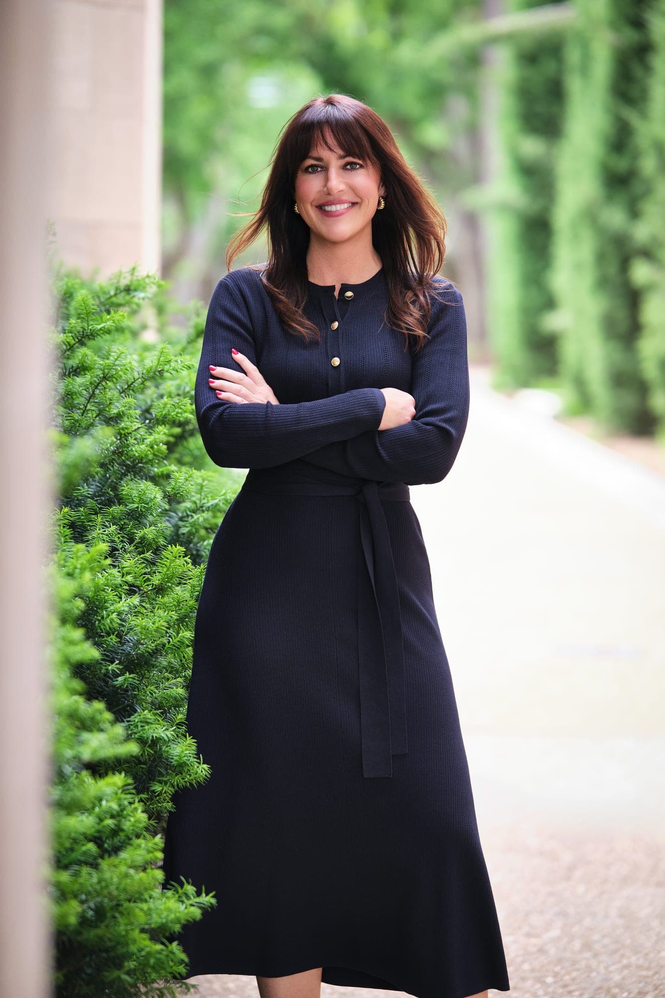 MHS Legacy marketing director Jessie Haupt in a navy midi dress beside a row of cypress trees at Washington University's Brookings Hall, photographed by Henry David Photography