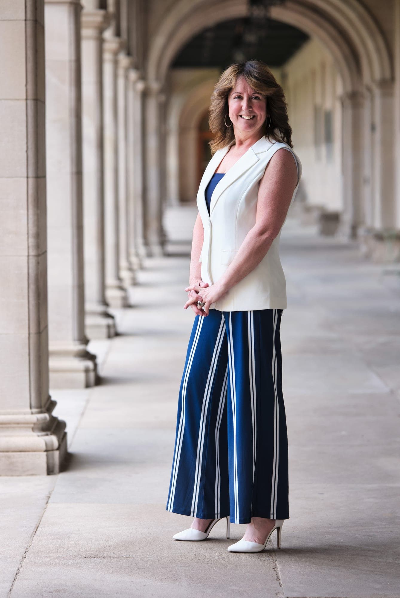Executive in a white sleeveless top and striped wide-leg trousers in a limestone arcade in St. Louis, by Henry David Photography